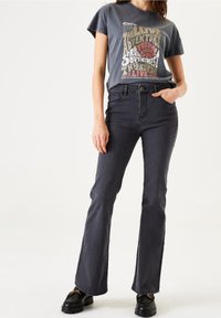 Mörkgrå utställda jeans med en slät textur, kombinerade med en grafisk t-shirt med flerfärgad text och en klassisk rundad halsringning.