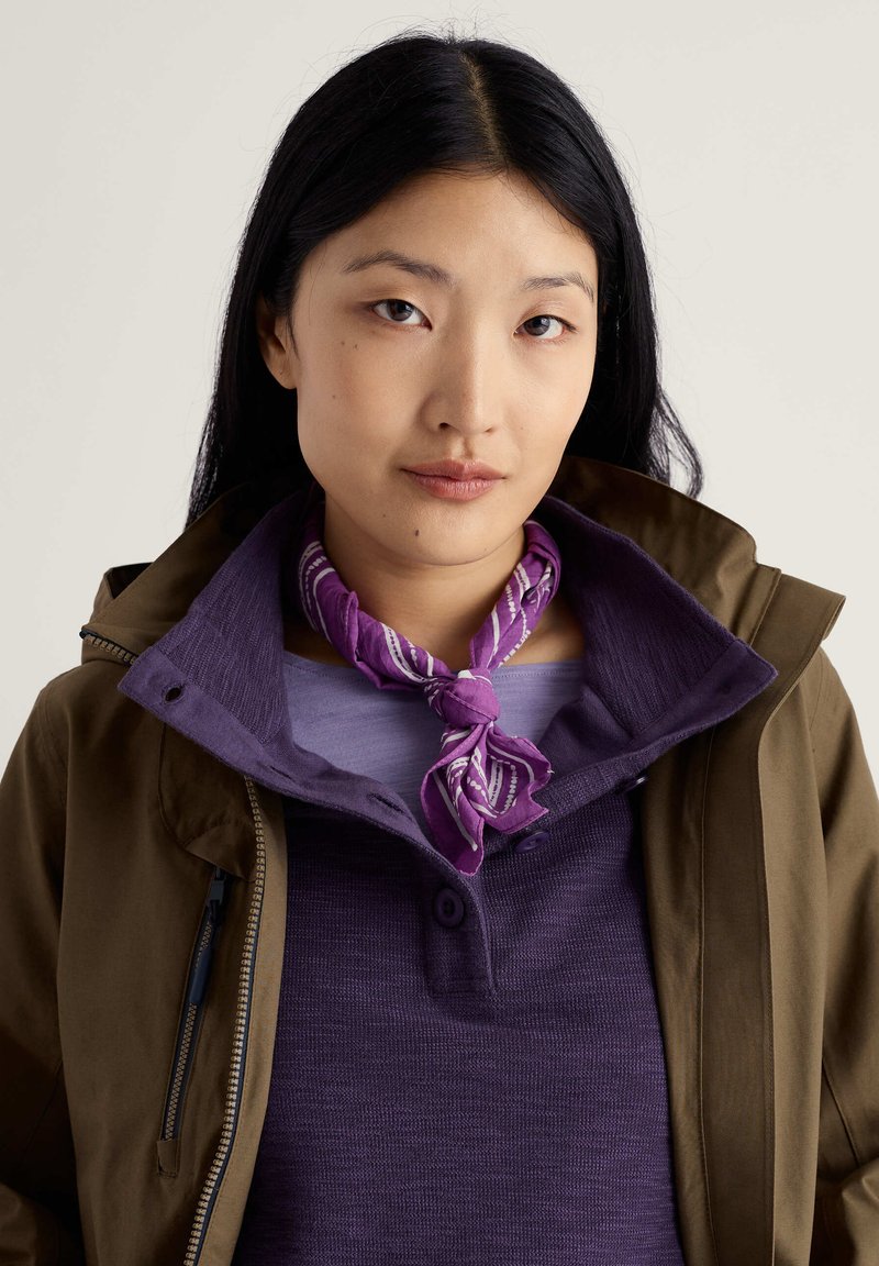 Brązowa kurtka na fioletowej teksturowanej koszuli z plisą na guziki, w zestawie z wzorzystym fioletowo-białym szalikiem zawiązanym na szyi.