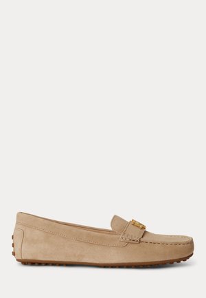 Mocassin beige en daim avec détail de boucle dorée, semelle cloutée en caoutchouc et coutures sur les côtés et l’avant, présenté de profil.