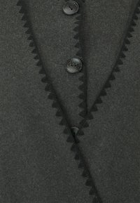 Gilet di lana grigio scuro con bordo smerlato lungo l'apertura frontale, due grandi bottoni neri e una superficie morbida e testurizzata.
