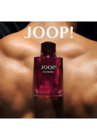Glasparfymflaska i rosa nyans med en mörk kork. Texten "JOOP! HOMME" i blått mot en ljus bakgrund. Synlig slät hud.