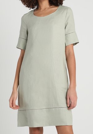 Femme portant une robe vert clair mi-genou avec des manches courtes et des détails subtils de couture horizontale près des manches et de l'ourlet.