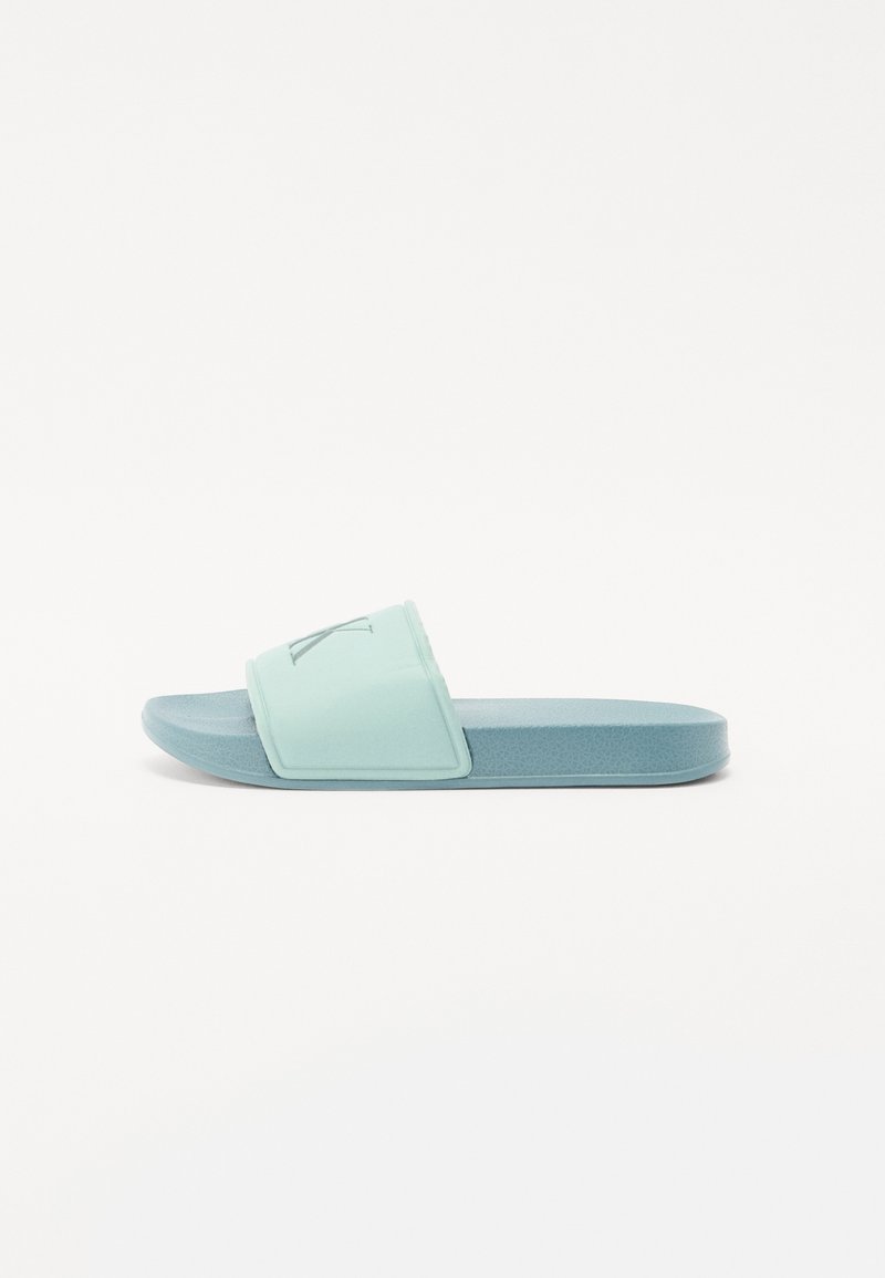 Helle blaue Rutschsandale mit einem strukturierten Oberriemen und einer flachen, gepolsterten Sohle. Verfügt über ein auffälliges Logo auf dem Riemen.