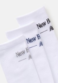 Three pairs of white ribbed crew socks with "New Balance" logo embroidered in gray, navy, and black near the cuff.