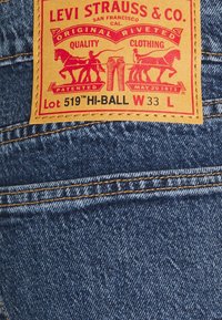Etiqueta de denim de Levi Strauss con ilustraciones en relieve de un caballo y un jinete. Cuero marrón claro con texto rojo y negro, cosido sobre tela azul.