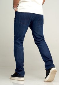 Mörkblå denimjeans med smal passform, utrustade med två bakfickor och en slät textur. Matchas med svarta sneakers och en vit T-shirt.