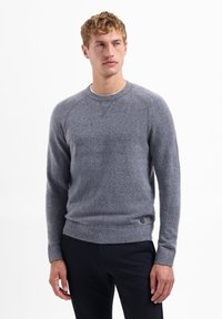 Grijze gebreide trui met een ronde hals en geribde zoom. Heeft een subtiele textuur en lange mouwen met raglannaden, gecombineerd met donkere broeken.