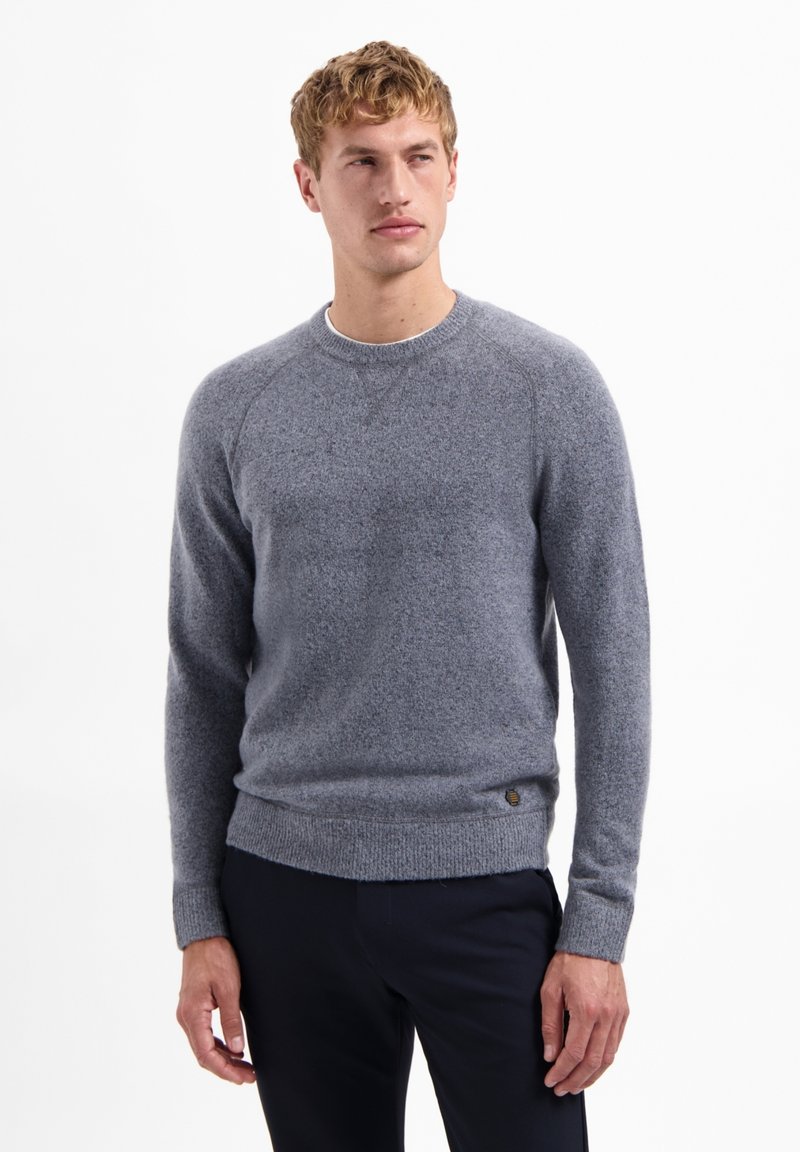 Grijze gebreide trui met een ronde hals en geribde zoom. Heeft een subtiele textuur en lange mouwen met raglannaden, gecombineerd met donkere broeken.