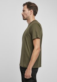 Camiseta de algodón verde oliva con mangas cortas y cuello redondo, exhibida en un modelo de lado. Diseño sencillo, sin patrones.