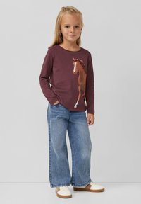 Bordeauxfarbendes Langarmshirt mit einem Pferde-Graphic, kombiniert mit weit geschnittenen blauen Jeans und weißen Sneakers mit braunen Akzenten.