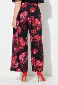 Široké květinové kalhoty z černé látky s velkými červenými a růžovými pivoňkami. Design má hladkou texturu a vysoký pas.