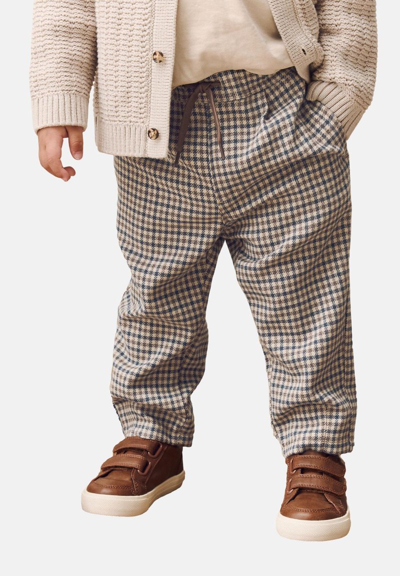 Braun karierte Hose mit lockerer Passform, ausgestattet mit einem elastischen Bund und seitlichen Taschen. Kombiniert mit braunen Sneakers mit Klettverschluss.