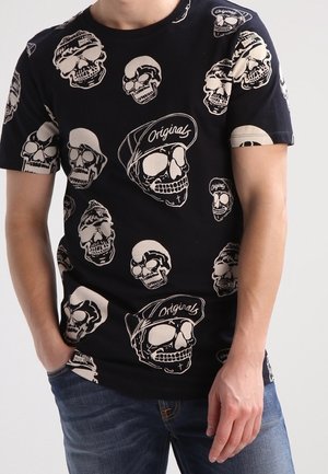 Camiseta de algodón negra con un patrón gráfico de calaveras repetido en beige, con el texto "Originals" en algunas calaveras. Diseño de mangas cortas y cuello redondo.