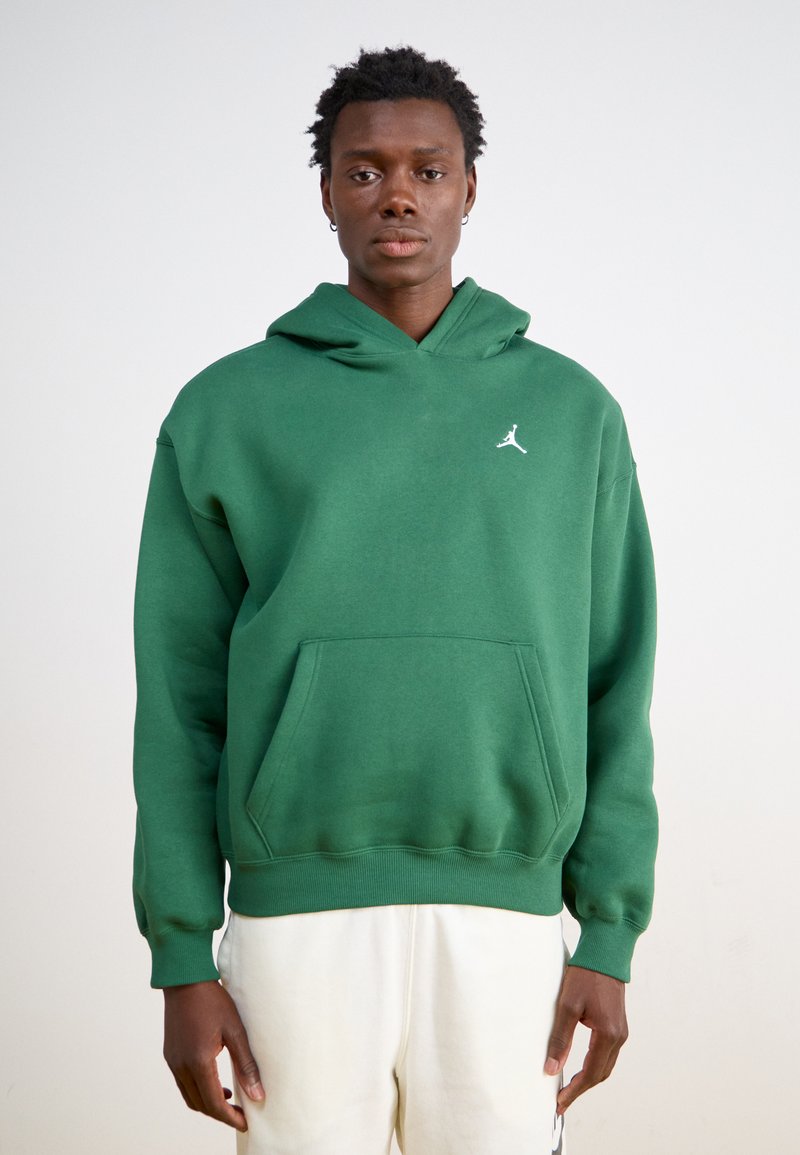 Zelená mikina s kapucňou vyrobená z mäkkého materiálu, s vreckom typu "kangaroo", rebrovanými manžetami a bielym logom Air Jordan na ľavej hrudi.