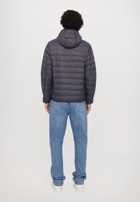 Grå pufferjakke med hette, med kviltet tekstur og en litt skinnende finish, kombinert med lyseblå jeans og hvite joggesko.