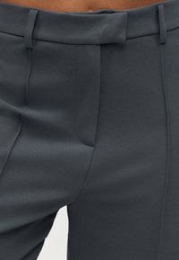 Γκρι παντελόνι σε στενή γραμμή με λείο, υφασμάτινο υλικό, καθαρές πιέτες στο εμπρός μέρος και μινιμαλιστικό σχεδιασμό στη μέση.