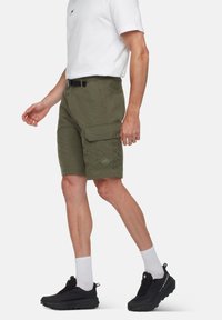 Olivgröna cargoshorts med flera fickor, bältesöglor och en märkespatch. Bärs med en vit t-shirt och svarta sneakers.