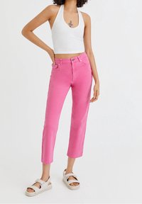 Jean en denim rose avec une coupe courte, taille haute et revers roulés, associé à un haut dos nu blanc côtelé et des sandales blanches.