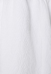 Tecido branco texturizado com um padrão amassado, apresentando linhas suaves e fluidas e um brilho sutil, criando uma aparência leve e arejada.
