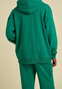 Groen sweatshirt met een capuchon, gemaakt van een katoenmix, met een losse pasvorm en geribbelde mouwen. Eenvoudig ontwerp zonder zichtbare patronen of accenten.