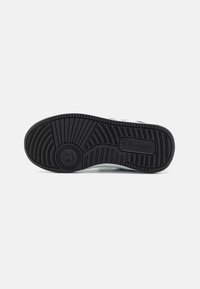 Semelle de chaussure en caoutchouc noir avec des motifs texturés et un logo circulaire, présentant des rainures profondes pour l'adhérence et la durabilité.