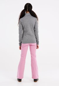 Grijze longsleeve top met hoge kraag, gecombineerd met roze uitlopende broek. Beide outfits zijn gemaakt van een gladde, rekbare stof en hebben een nette pasvorm.