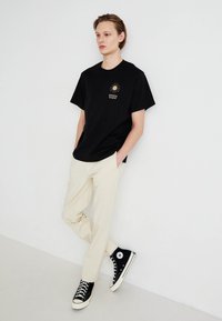 Tricou negru din bumbac cu un grafic mic de soare și eticheta "Levi's", asortat cu pantaloni lejeri de culoare crem și sneakers negri cu glezna înaltă.