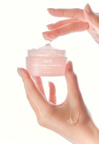 Maschera notturna al collagene PDRN di Abib in un barattolo trasparente e rotondo con una sfumatura rosa. La formula gelatinosa viene versata dalle dita su una mano.