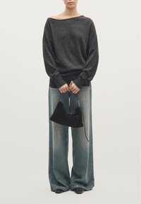 Dark gray oversized sweater with wide neckline, paired with light blue wide-leg jeans. Holding a small black suede handbag.