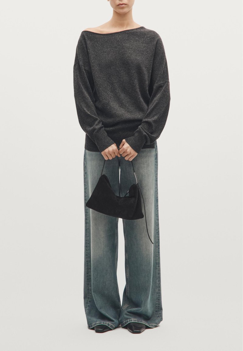 Maglione oversize grigio scuro con scollatura ampia, abbinato a jeans a gamba larga blu chiaro. Tiene una piccola borsa in suede nera.