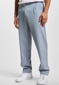 Lichtblauwe plooibroek met verticale strepen, voorzien van een elastische tailleband en trekkoord, gecombineerd met witte sneakers.