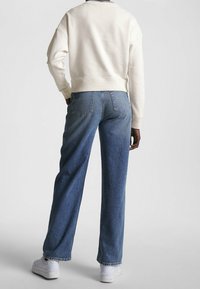 Felpa crema con spalle cadenti, abbinata a jeans blu a vita alta e dritti. Sneakers bianche completano l'outfit.