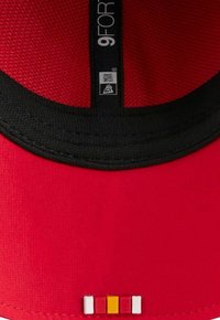 Roter Hut mit schwarzen Akzenten, Obermaterial aus Mesh-Stoff, gebogener Schirm und ein gemustertes Detail mit vier farbigen Quadraten auf der Vorderseite.