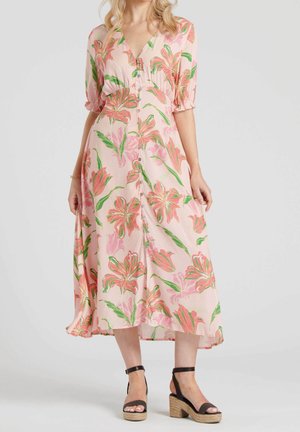 Femme portant une robe midi boutonnée rose à fleurs avec des manches bouffantes et des sandales à plateforme noires à bride à la cheville, sur un fond uni.