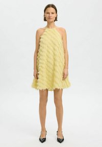 Yellow halter-neck dress with layered, textured fringe; flared shape; above-knee length; worn with black pointed-toe heels.