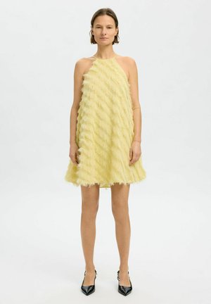 Yellow halter-neck dress with layered, textured fringe; flared shape; above-knee length; worn with black pointed-toe heels.