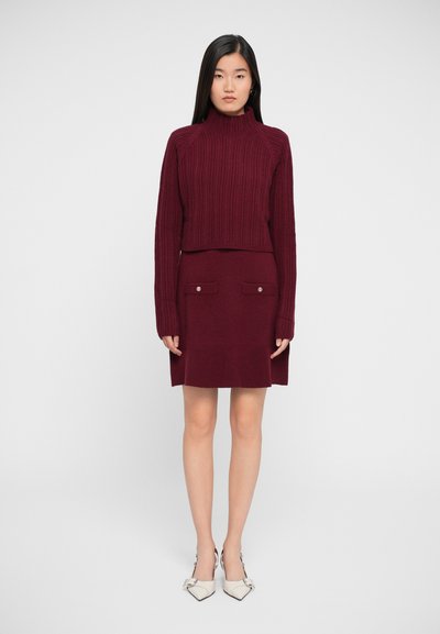 Burgundy ribbed knit sweater with high collar paired with a matching skirt featuring two front pockets and button accents.