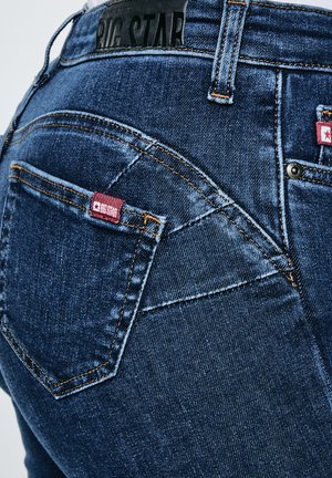 Detailní záběr zadní kapsy modrých džínů z denimu s červenou značkou Big Star a černou koženou nášivkou s logem na pásku kalhot.