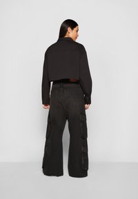 Black cropped jacket with a pointed collar, paired with wide-leg black cargo pants featuring multiple side pockets and a faded texture.