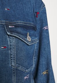 Spijkerjack met blauwe stof, voorzien van twee voorzakken, zilverkleurige hardware en kleurrijke geborduurde accenten in rood, roze en geel.