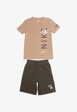 T-shirt en coton beige avec un logo vertical "NIKE" en marron et blanc, accompagné d'un short en coton vert foncé avec un logo blanc.