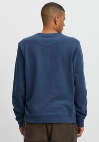 Marineblå sweatshirt laget av mykt materiale, med lange ermer, rund hals og ribbet kant. Bakvisning viser minimal detaljer.