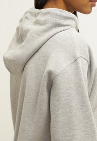 Szary bawełniany hoodie o miękkiej fakturze, z dużym kapturem, luźnym krojem i minimalistycznymi detalami szycia na szwach.