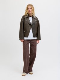 Brown leather biker jacket with silver hardware, white t-shirt, and wide brown striped pants. Model stands against a light background.