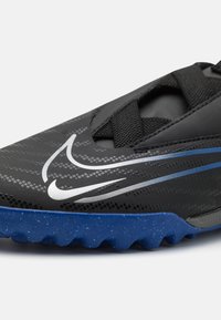 Musta synteettinen urheilukenkä, jossa on teksturoitu päällinen, sininen kumipohja, jossa on pilkullista yksityiskohtaa, ja hopeinen swoosh-logo.