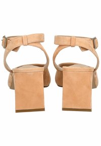Sandalias de tacón de ante beige con tira en el tobillo. Tacón cuadrado grueso y suela suave. Presenta una hebilla metálica para un cierre seguro.