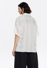 Short-sleeve, striped shirt in light colors, with vertical gray and white lines, featuring a button-up collar and relaxed fit design.