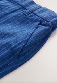 Tela a rayas azules, con una textura suave y un brillo sutil. Incluye bolsillo lateral y costuras visibles en el dobladillo.