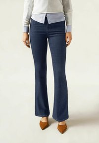Mörka denim flare-jeans med hög midja, subtila sömmar och en slät textur, i kombination med bruna spetsiga skor.
