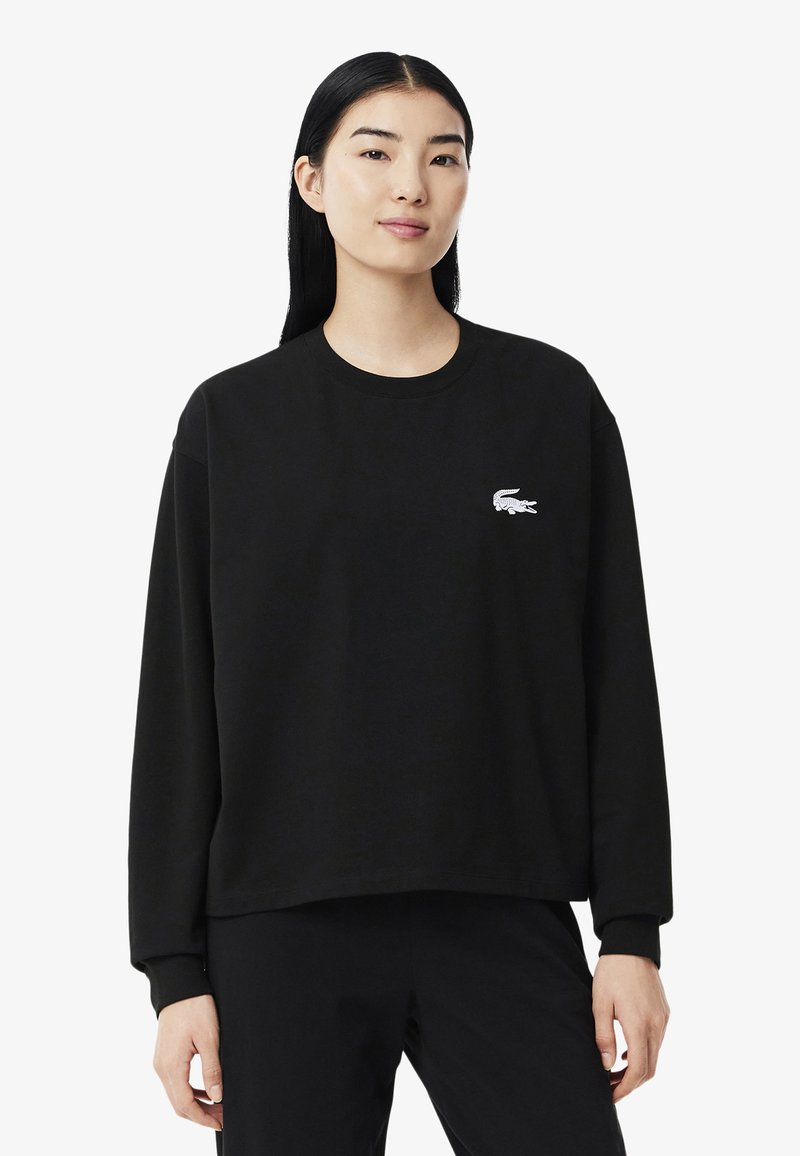 Sweatshirt de algodão preto com mangas longas, gola redonda e um logo bordado branco no lado esquerdo do peito. Textura suave e corte descontraído.